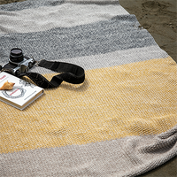 Striped knitted throw blanket with a camera and book on a sandy surface