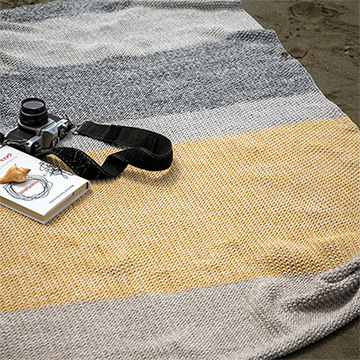 Striped knitted throw blanket with a camera and book on a sandy surface