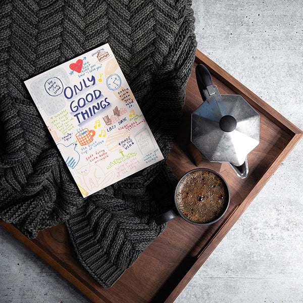 Book titled 'Only Good Things' on a wooden tray with a cup of coffee, coffee maker, and dark grey washed chevron throw.