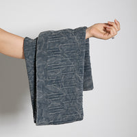 Person holding a folded flintstone and blue folded washed blanket with a subtle pattern against a plain background.