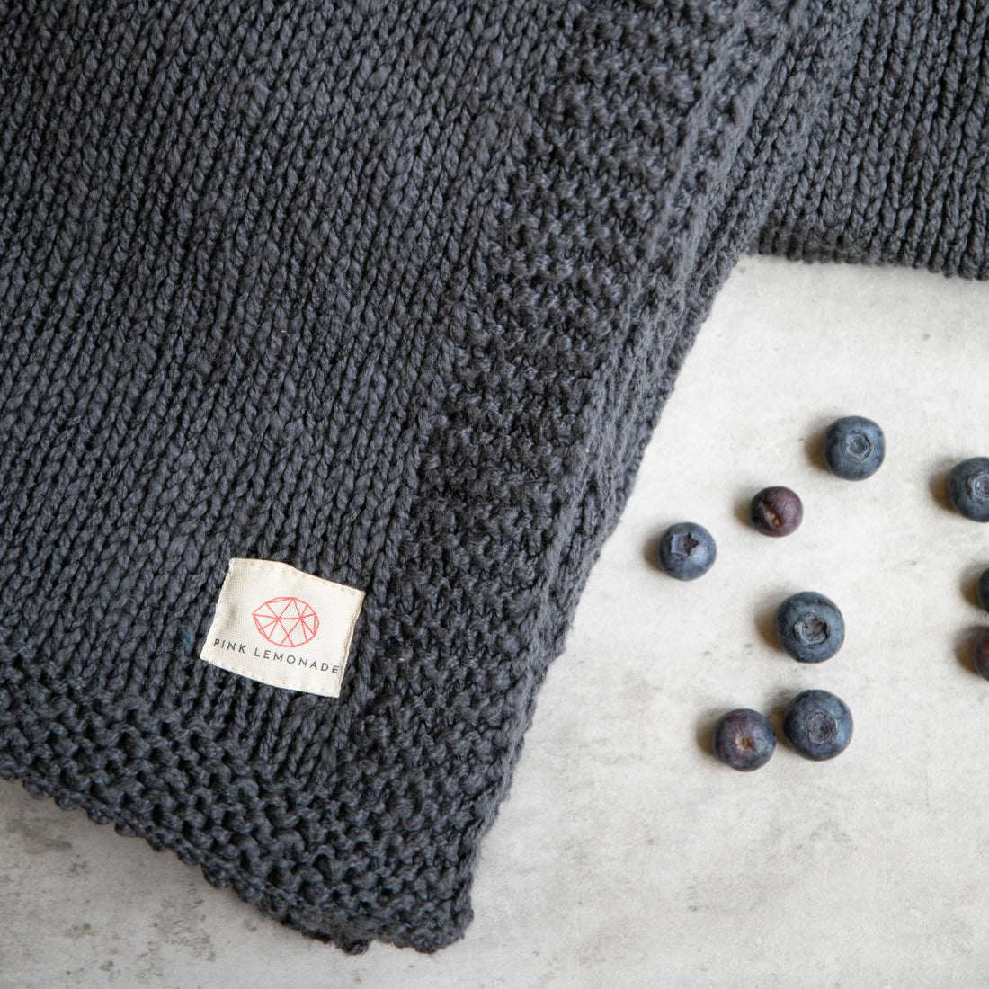 Close up of the Zrestha organic cotton throw with a few blueberries scattered on a white surface.