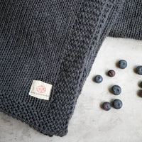 Close up of the Zrestha organic cotton throw with a few blueberries scattered on a white surface.