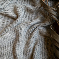 A close up of a linen coloured cotton throw with wooden shavings in the background.