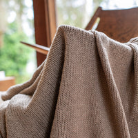 Close-up of a grey stone knitted cotton blanket draped over a wooden chair.