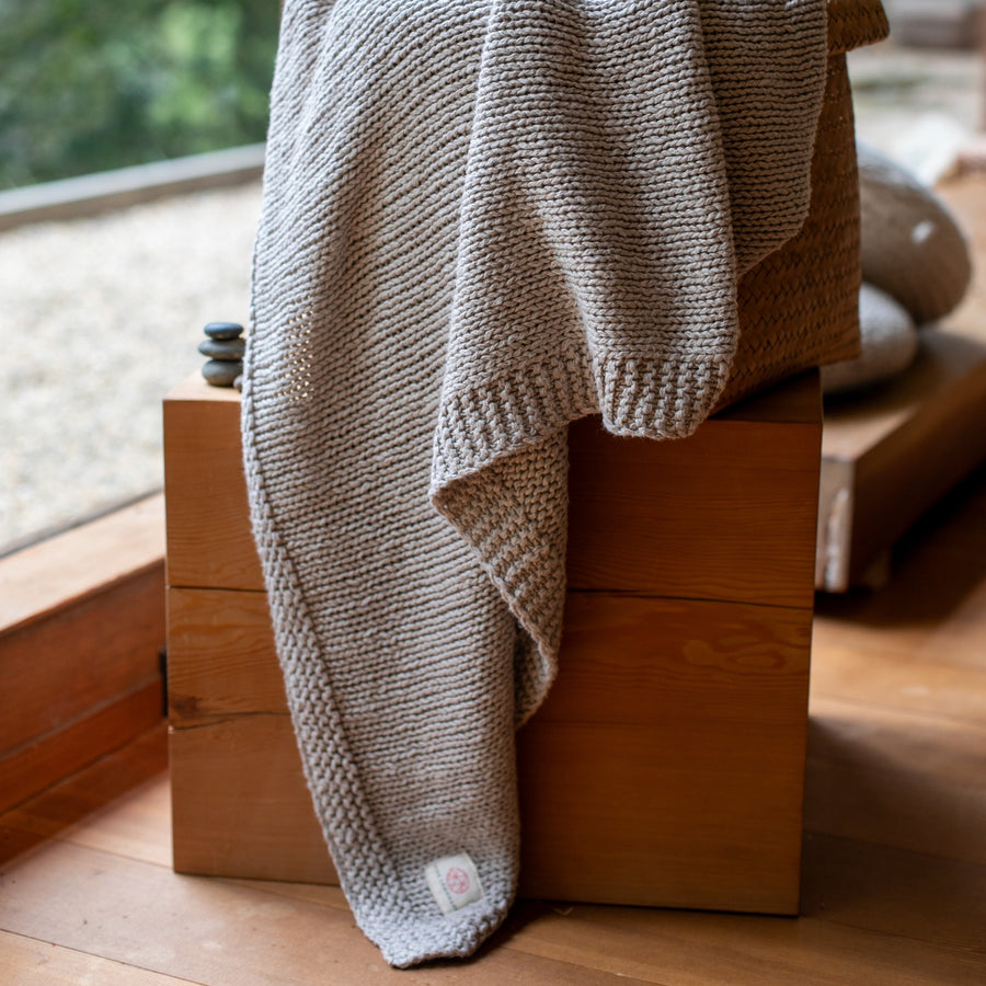 Stone grey knitted throw blanket hanging on top of a wooden box.