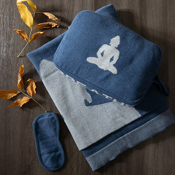 Set of marine blue and gray cotton travel blanket and pouch with a buddha design with a matching eye mask on a wooden surface.