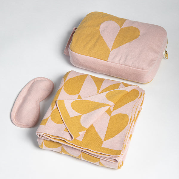 Pink and mustard patterned cotton blanket with matching pouch and eye mask on a light gray background.