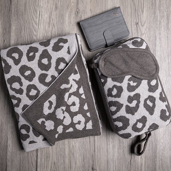 Brown leopard print travel set including a blanket, pouch, and eye mask on a wooden surface with a card holder.