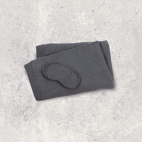 Dark organic cotton gray eye mask and folded gray blanket on a light textured surface.