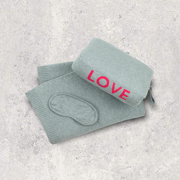 Light grey travel blanket set with 'LOVE' in red with a matching eye mask on a textured gray surface.
