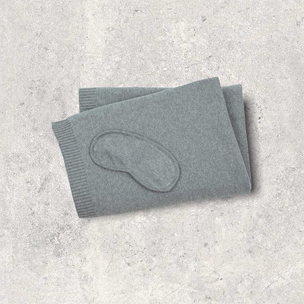 Medium grey eye mask and folded organic cotton blanket on a textured gray surface.