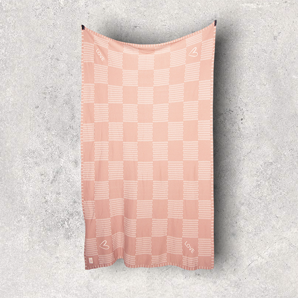 Pink checkered cotton travel blanket hanging on a gray textured background