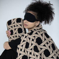 Woman wearing a black eye mask and a patterned black and beige blanket while holding a matching blanket cover against a white background