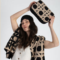 Woman holding a geometric-patterned black travel pouch with a matching cotton blanket wrapped around her.