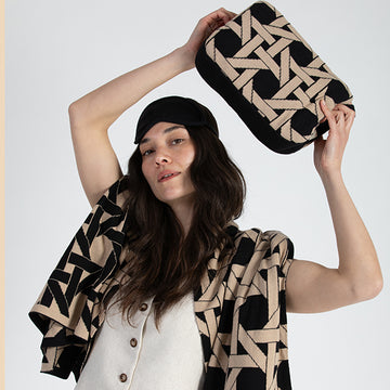 Woman holding a geometric-patterned black travel pouch with a matching cotton blanket wrapped around her.
