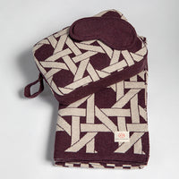 Folded burgundy blanket with geometric pattern and matching eye mask on a light gray background.