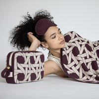Woman using Riti geometric organic cotton travel blanket and eye mask travel set in burgundy, soft compact travel gift for women.