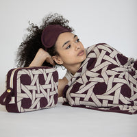 Woman wrapped in a patterned burgundy and white blanket with a matching bag on a plain background