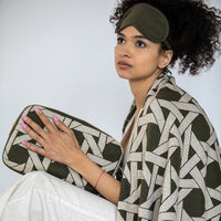 Woman wrapped in a patterned olive green cotton blanket and holding a matching pouch against a white background.