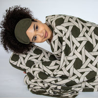 Woman wrapped in a green and beige geometric patterned blanket on a white background.