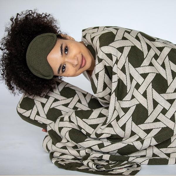 Woman wrapped in a green and beige geometric patterned blanket on a white background.