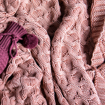 Close-up of a pink curvy knitted cotton blanket with a purple knitted wine sleeve.