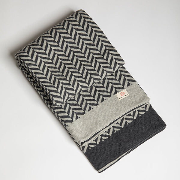 Grey folded organic cotton blanket with a herringbone pattern on a light gray background.