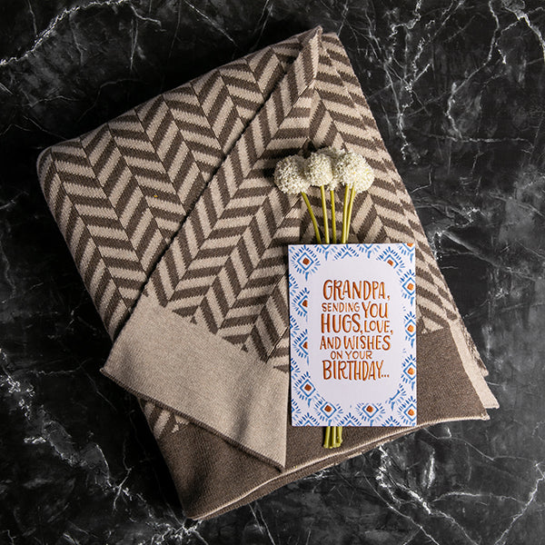 Folded dark brown and beige patterned cotton throw blanket with a birthday card addressed to Grandpa.