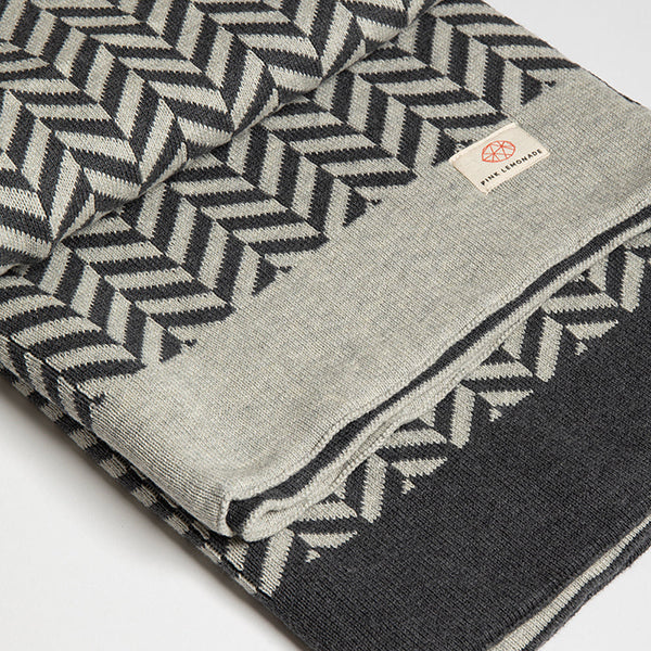 Folded dark grey organic cotton throw with a geometric herringbone pattern and a 'Pink Lemonade' brand label.